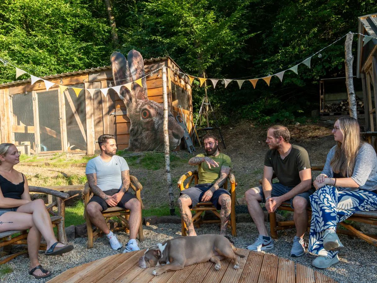 Gruppe sitzt gemeinsam im Kreis auf dem Hof, Hund liegt dabei